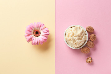 Shea butter with nuts and flower on color background