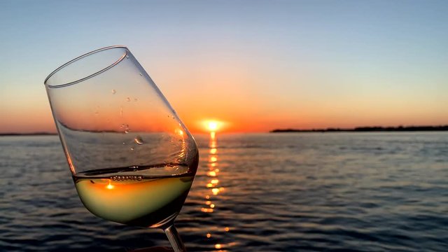 A glass of white wine during the beautiful sunset in Pula Croatia. The sun is orange.