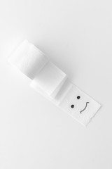 Proctology concept with toilet paper roll and painted face on white background top view
