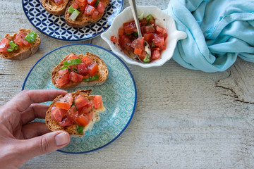 Top view of woman hands preparing tasty tomato Italian appetizers -  bruschetta, on slices of toasted baguette, close up view.