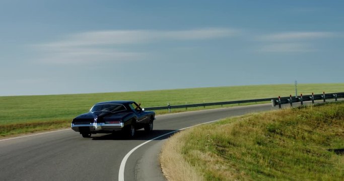 TRACKING Old classic vintage 70s muscle car driving thorough rural landscape. 4K UHD RAW graded footage
