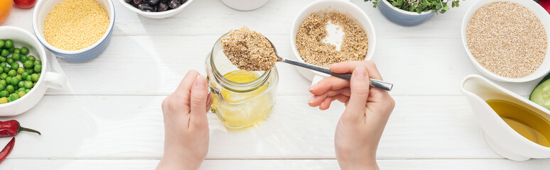 cropped view of woman adding couscous in jar with oil on wooden white table, panoramic shot