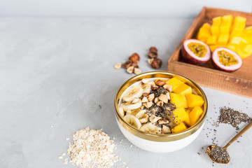 Breakfast oatmeal porridge with fresh fruits, chia seeds and hazelnut on gray background. Oatmeal with mango and banana. Healthy breakfast concept. Mockup, overhead, copy space