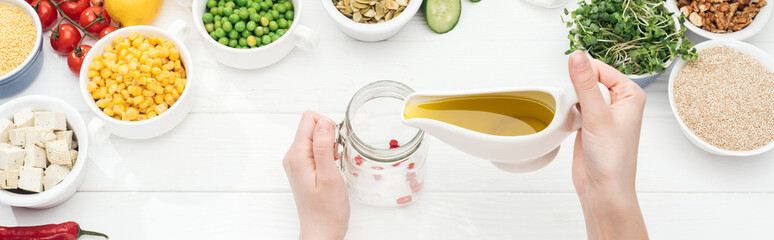 partial view of woman adding oil in glass jar on wooden white table, panoramic shot