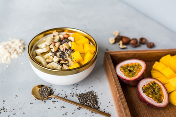 Breakfast oatmeal porridge with fresh fruits, chia seeds and hazelnut on gray background. Oatmeal with mango and banana. Healthy breakfast concept. Mockup, overhead, copy space