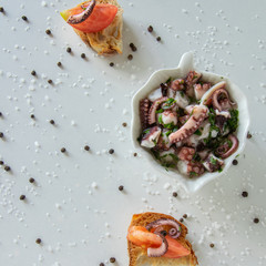 Top view of octopus salad with slices of toasted baguette - bruschetta  on white background with black pepper and sea salt. Typical Mediterranean .appetizer food.