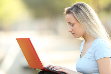 Serious teenage girl using a red laptop in a park