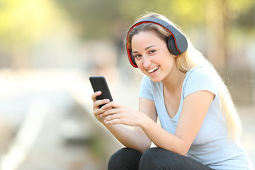 Happy teenage girl holding a smart phone looking at you