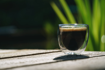 Small transparent double wall glass cup of fresh brewed coffee placed on a natural wooden surface