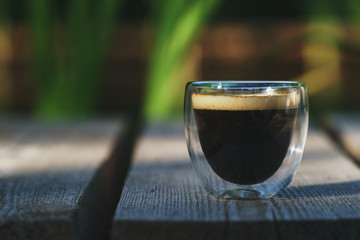 Small transparent double wall glass cup of fresh brewed coffee placed on a natural wooden surface
