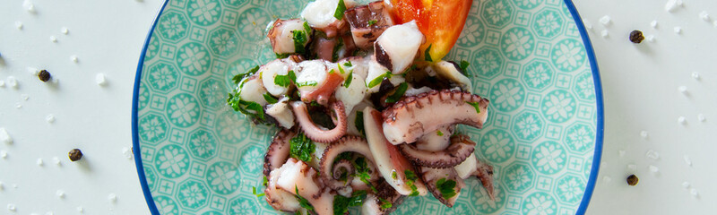 Top view of octopus salad, typical Mediterranean food, on white background with black pepper and sea salt