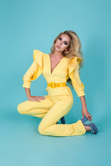 Elegant blonde woman in stylish yellow jumpsuit and fashionable accessories on color background. Beautiful fashion model on blue background.