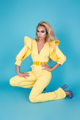 Elegant blonde woman in stylish yellow jumpsuit and fashionable accessories on color background. Beautiful fashion model on blue background.
