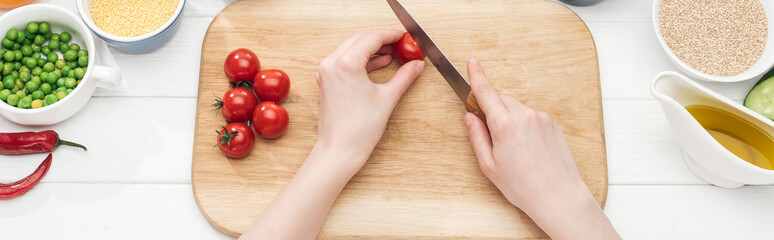 cropped view of woman cutting cherry tomatoes on wooden chopping board, panoramic shot