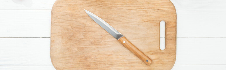 panoramic shot of wooden chopping board with knife on white table