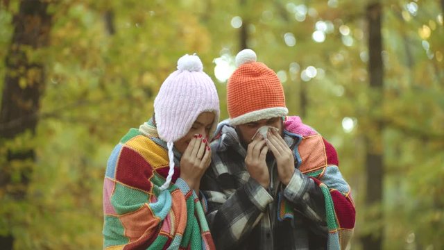 Young coule blowing nose at nature. Cold flu season, runny nose. Showing sick coule sneezing at autumn park.