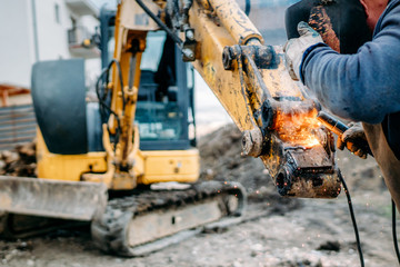 Professional worker welding excavator arm on construction site