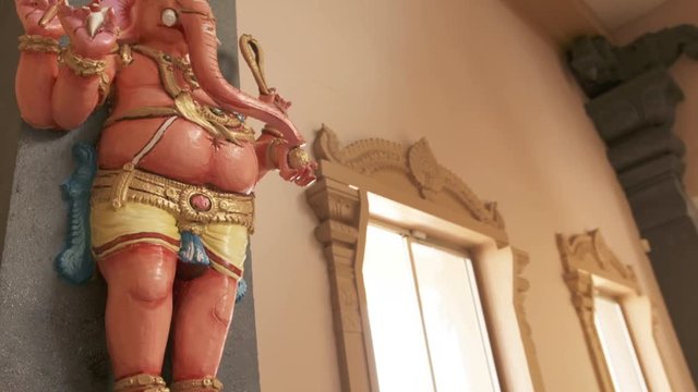 Handheld, medium close up shot of a small Ganesha statue on the wall.