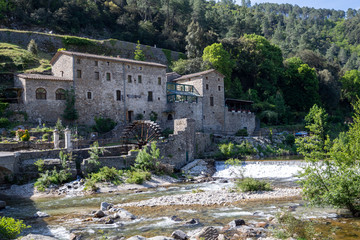 Fototapeta na wymiar Eine historische Herberge in den französischen Cevennen mit einem Fluss und einem Wehr im Vordergrund