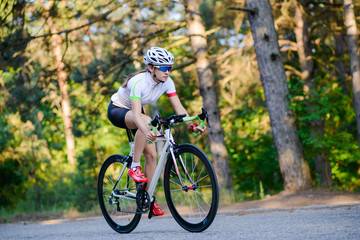 Naklejka premium Young Woman Cyclist Riding Road Bicycle on the Free Road in the Forest at Hot Summer Day. Healthy Lifestyle Concept.