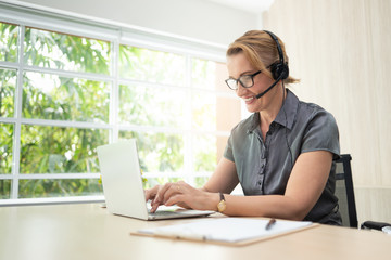 Smiling woman in working on laptop and headset in call center.