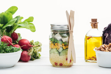 fresh vegetable salad in glass jar near oil and radish isolated on white