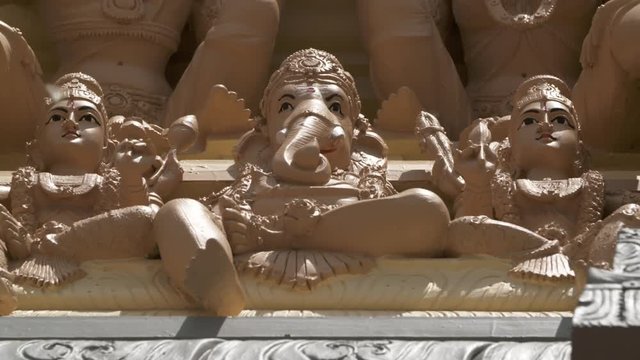 Handheld, low angle, medium close up shot of a Ganesha statue on the exterior wall of the Hindu temple.
