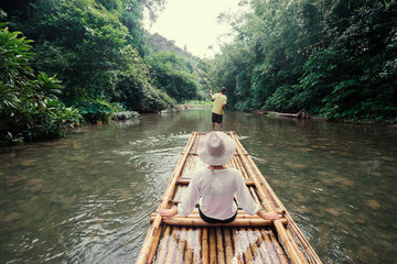 Traveling by Thailand. Back view of tourist enjoying view sailing jungle river on traditional bamboo raft.