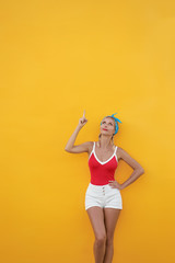 Your text here. Cheerful beautiful young woman pointing up while standing against yellow wall.