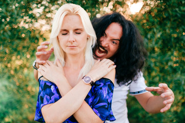 Fototapeta premium Funny couple outdoor. Odd people. Crazy italian man frightening from behind praying woman with closed eyes.