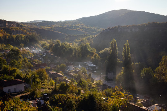 Aerial view of beautiful foggy village between mountains in Lovech, Bulgaria. Misty sunrise view of city district surrounded by rock mountain. Sun beams between trees © CrispyMedia