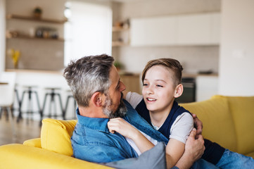 Fototapeta premium Mature father with small son sitting on sofa indoors, resting.