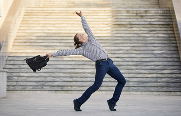 Crazy young businessman dancing on the street with bag. Celebrating victory. Flexibility and grace...