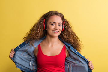 Portrait of a young woman with headphones in a studio on a yellow background.