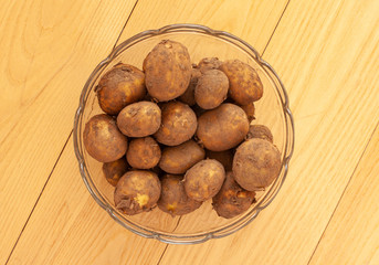 Pile of fresh new raw potatoes with peel on in a glass bowl. Close up on wooden background. - Image