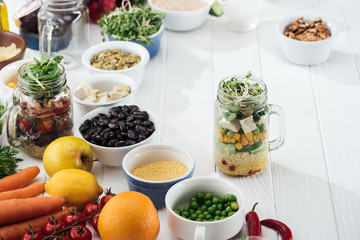 ingredients in bowl near glass jars with salad on wooden white table