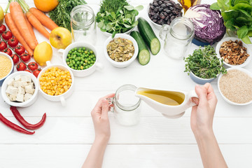 cropped view of woman adding sauce in empty glass jar on wooden white table