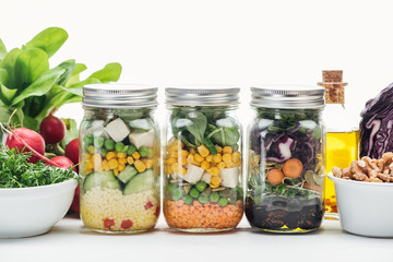 fresh vegetable salad in glass jars near oil and radish isolated on white