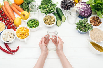 cropped view of woman holding empty glass jar on wooden white table