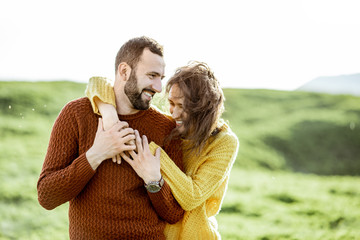 Portrait of a lovely couple dressed in bright sweaters hugging on the green meadow while traveling...