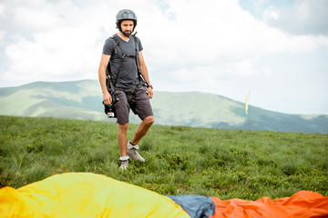 Well-equipped man preparing for the paraglider flight, standing on the green meadow high in the mountains