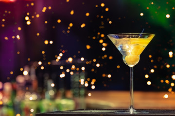 Martini at the bar counter. Classic cocktail in the bar. Dark background with neon lights and festive bokeh. Focus on the liquid. Horizontal