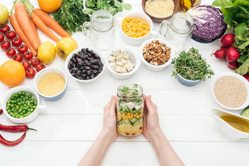 cropped view of woman on holding glass jar with salad on wooden white table
