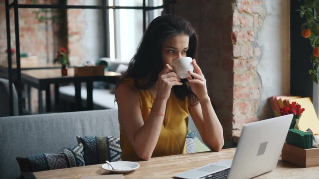 Beautiful young woman in trendy garment is drinking coffee in cafe enjoying solitude and tasty drink sitting at table alone thinking looking out of the window.