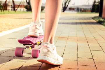 Young girl in comfortable speakers using pink skateboard for riding