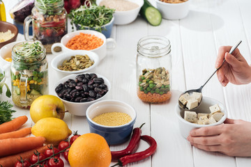 cropped view of woman adding tofu cheese in glass jar on wooden white table