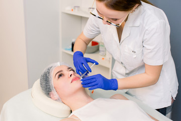 The doctor cosmetologist makes Lip augmentation procedure of a beautiful woman in a beauty salon....