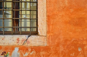 old terracotta wall with cracks and scuffs and part of the window with bars