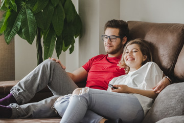 A young couple watches television on the couch at home