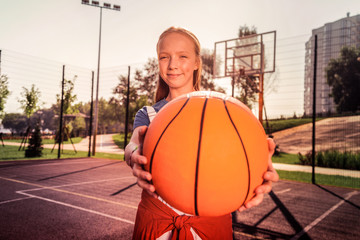 Positive pretty teenage girl having unusual hobby and playing basketball